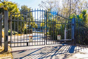 Secure entrance to a property, surrounded by lush greenery and a paved driveway.