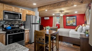 A kitchen with wooden cabinets, a stainless steel refrigerator, a microwave, and a stove. There is a dining area with a table and chairs, and a red wall in the background. - 19 Creekside Retreat (Sedona)