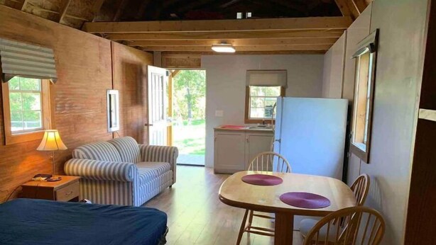 Ein gemütliches Zimmer mit einem Bett, einem gestreiften Sofa, einem Esstisch mit Stühlen, einer Lampe und einem Kühlschrank.