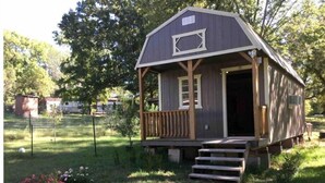 Eine kleine Holzhütte mit einer Veranda und Treppen, die zum Eingang führen.