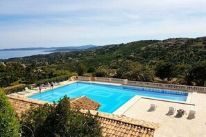 Relax by the serene pool surrounded by lush greenery and a distant sea view.