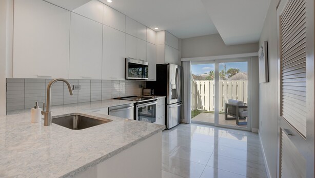 A modern kitchen with a large island, stainless steel appliances, and a sliding glass door leading to an outdoor patio.