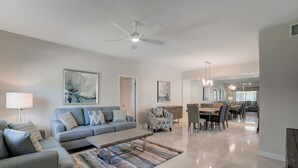 A modern living room with a sofa, coffee table, and patterned rug. There is a dining area with a table and chairs.