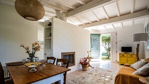 A dining area with a wooden table, chairs, and a vase of flowers. There is a fireplace and a yellow cabinet with a television. - Villa il Sogno - Homelike Villas (Ostra Vetere)