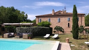 A pool with lounge chairs, a covered seating area, and a brick building with shutters. - Villa il Sogno - Homelike Villas (Ostra Vetere)