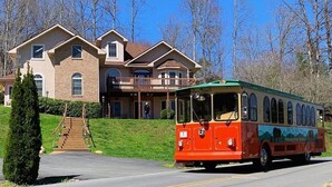 A red and yellow trolley bus parked in front of a large house with a balcony.