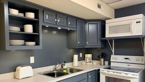 A compact kitchen with grey cabinets, a white microwave, a stove, and a sink.