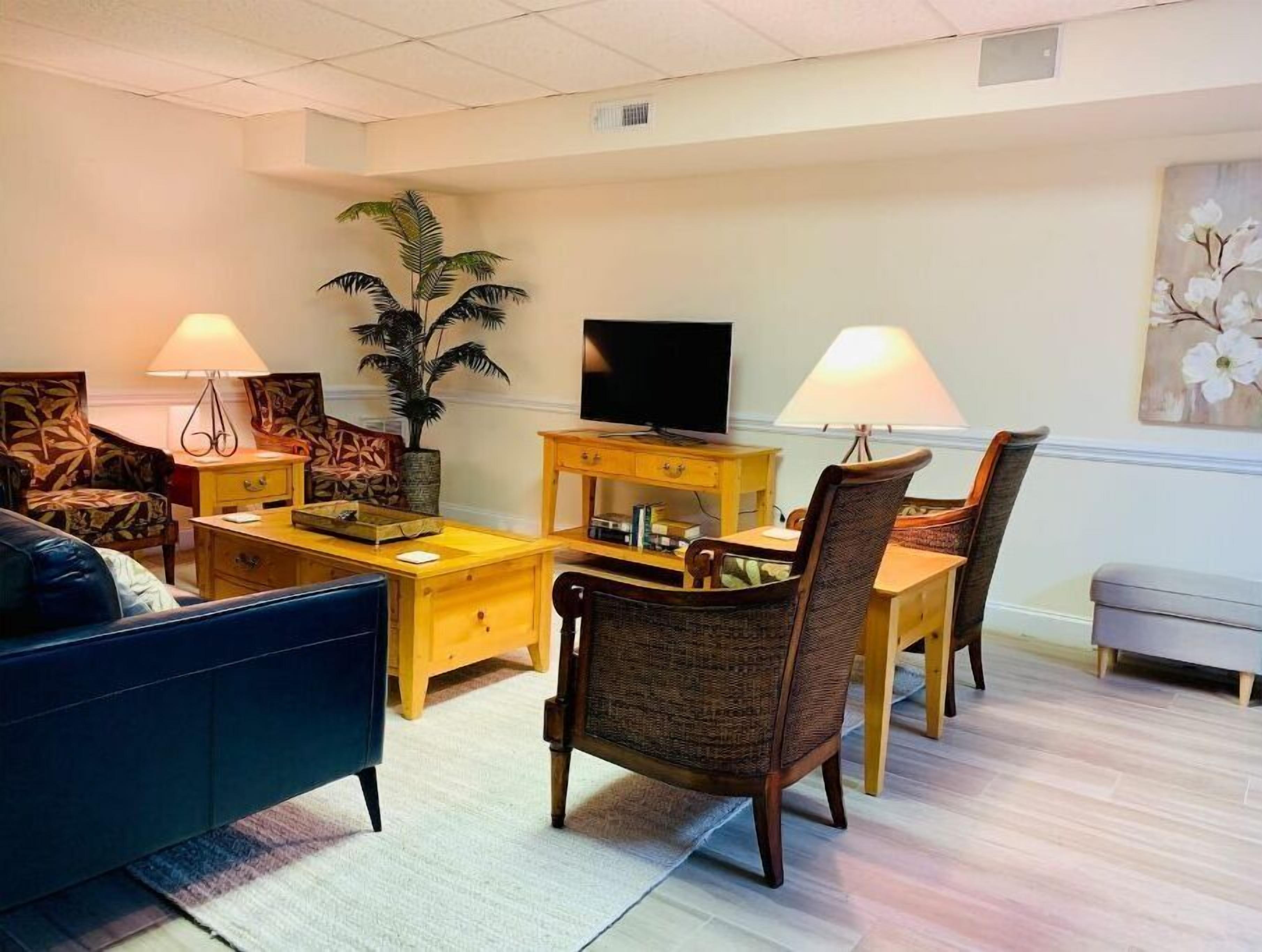Una sala de estar moderna con un sofá, dos sillones, una mesa de centro, un televisor y una mesa de comedor con sillas. Hay dos lámparas a cada lado de la habitación.