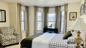 A bedroom with a large bed, a chair, a desk, and a lamp.