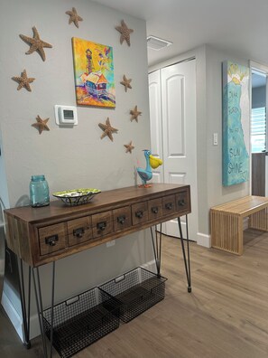 A room with a wooden console table, starfish wall decor, a painting, and a door with a 'Dear Florida, You are my sun shine' sign. - Stunning Views at Mariner Pointe 541 (Sanibel)