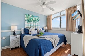 Quarto com uma cama, um ventilador de teto, um quadro, uma TV e uma mesinha de cabeceira.