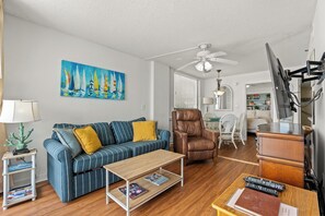 Uma sala de estar com sofá, poltrona, mesa de centro e um quadro de veleiros.