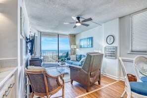 A spacious balcony with a view of the ocean, a ceiling fan, and a dining area with a table and chairs.