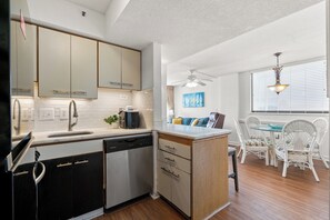 A kitchen with white cabinets, a dishwasher, and a dining area with white wicker chairs and a glass table.