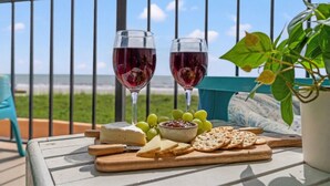 A balcony with a view of the beach, two glasses of red wine, cheese, grapes, crackers, and a potted plant. - Carolina Reef 101 - 2 Bedroom Ocean Front Condo (North Myrtle Beach)
