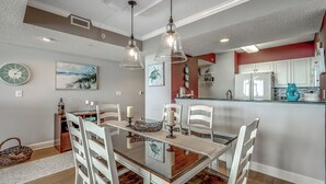 Un espace repas avec une table en verre, des chaises blanches, des luminaires suspendus et un mur d’accent rouge.