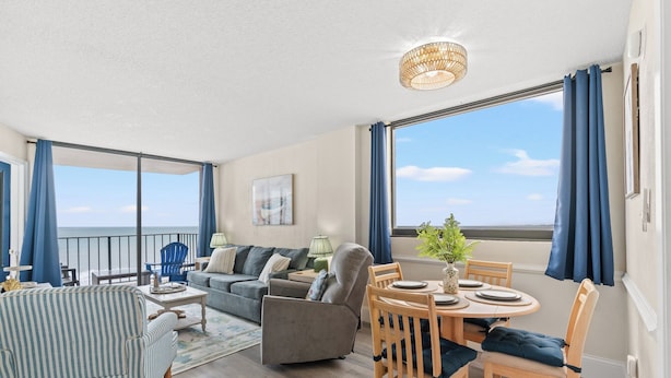 Amplia sala de estar con balcón, una mesa de comedor preparada para cuatro personas y un sofá con vista al mar.