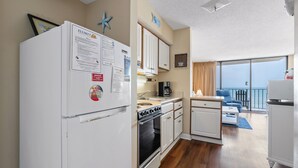 Eine kompakte Küche mit Kühlschrank, Herd und Spüle, ein Essbereich mit Tisch und Stühlen sowie ein Balkon mit Blick.