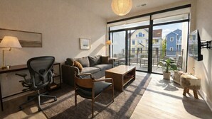 Ein modernes Wohnzimmer mit einer Couch, einem Couchtisch und Sesseln, einem Schreibtisch mit Lampe sowie einem großen Fenster mit Blick auf Gebäude.