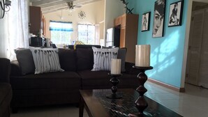 Una sala de estar con un sofá de color oscuro, dos lámparas decorativas y una mesa de centro estampada.