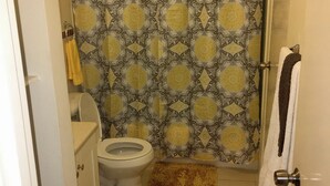 Un baño con cortina de ducha estampada, inodoro, lavamanos y dos alfombras.