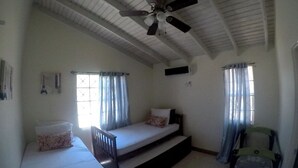 Una habitación con cama, una silla, ventilador de techo y ventana con cortinas.