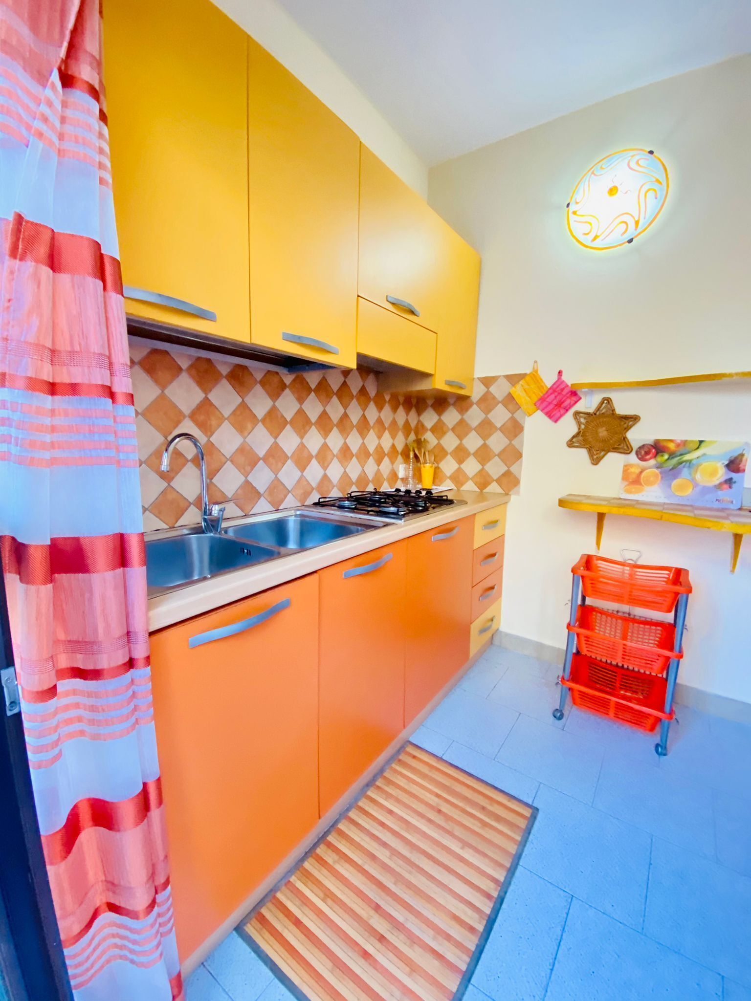 Una cocina con gabinetes naranja, un lavamanos y una estufa. Hay una decoración en forma de estrella en la pared y una exposición de frutas.