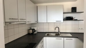 Una cocina moderna con armarios blancos, encimera negra, lavaplatos integrado y cafetera.