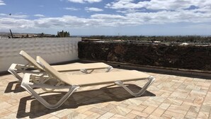 Terraza en la azotea con dos sillones color beige y un muro de piedra.