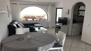 A compact living space with a dining table, a sofa, a TV, and a kitchen area.