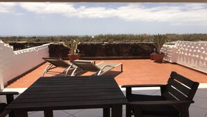 A rooftop terrace with a table and chairs, potted plants, and a view of the sea.