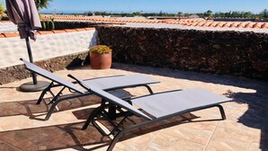 Terraza en la azotea con dos sillones, una planta en maceta y una pared de piedra.