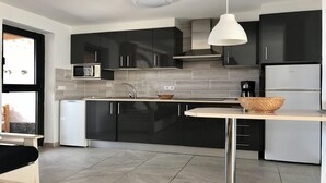 Una cocina moderna con armarios negros, un refrigerador blanco, un microondas y una lámpara colgante.