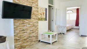 A hotel room with a flat-screen TV mounted on the wall, a small table with a green cloth, a white folding table, and a bed with a floral bedspread. - Welooveyou Lyra starlight B24 (Costa Calma (incl. Urbanización Cañada del Río))
