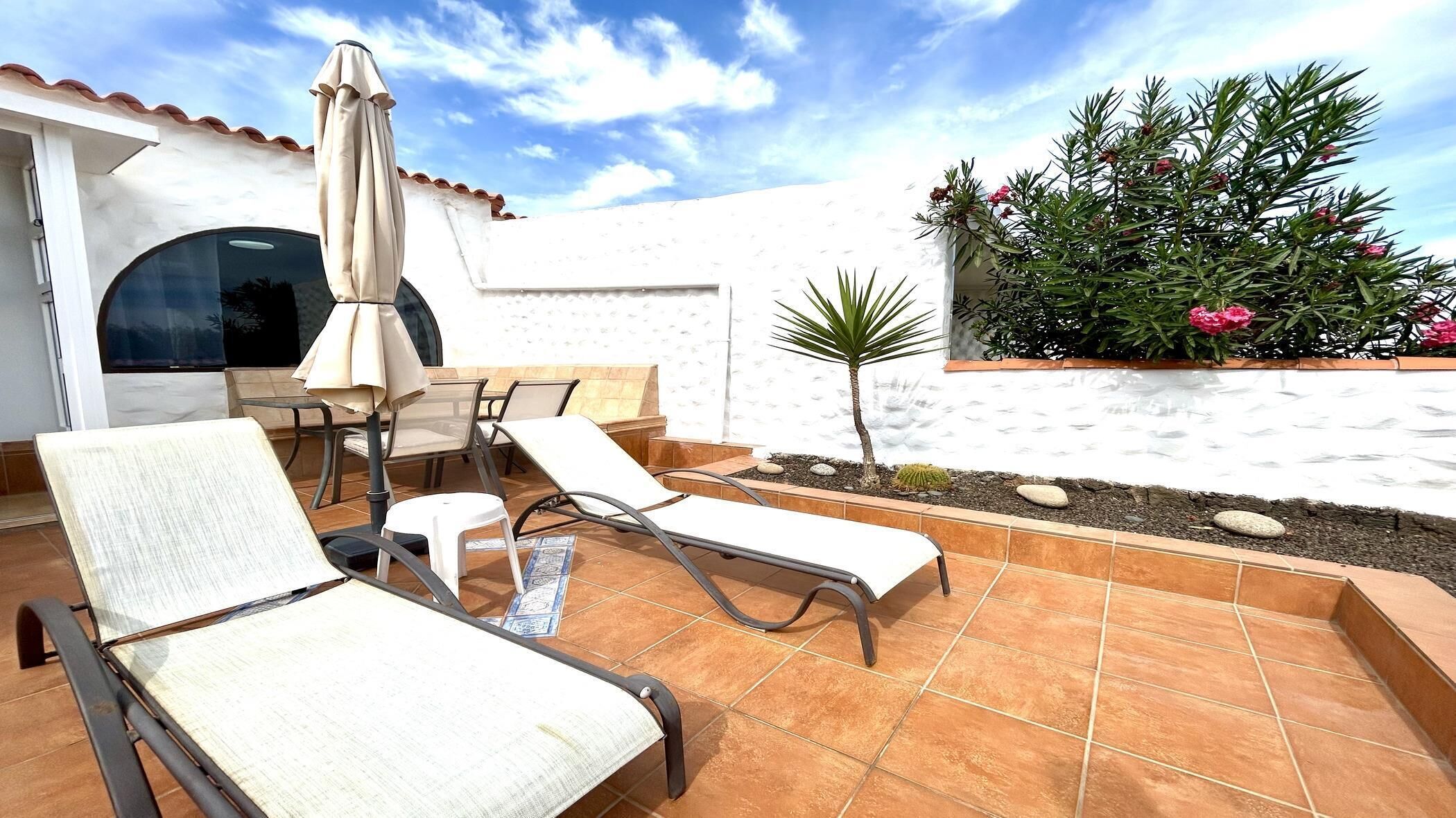 A patio with two lounge chairs, a table, and an umbrella.
