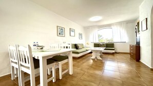 En moderne stue med spiseplads, sofa, sofabord og et vindue med gardiner.