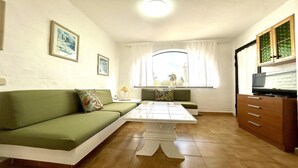 En kompakt opholdsstue med en grøn sofa, et lille bord, et fjernsyn på et træskab og et vindue med gardiner.