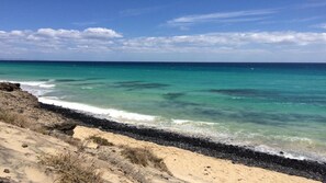 A beach with clear turquoise water, a rocky shoreline, and a sandy area with sparse vegetation. - Welooveyou Volans B30 (Costa Calma (incl. Urbanización Cañada del Río))