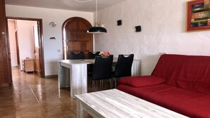 Una sala de estar con un sofá rojo, una mesa de comedor con cuatro sillas, una puerta de madera y un reloj de pared.