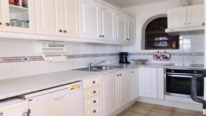 Una cocina con armarios blancos, un lavamanos de acero inoxidable, horno empotrado y cafetera.