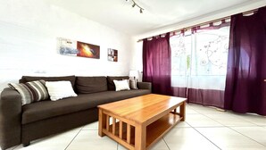 Ein Wohnzimmer mit einer Couch, einem Holztisch und einem Fenster mit violetten Vorhängen.