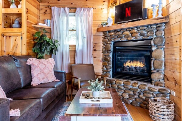 Un intérieur de chalet chaleureux avec une cheminée en pierre, un canapé en cuir et une table basse en bois.