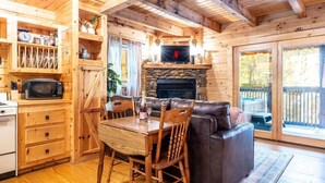 A cozy cabin interior with a stone fireplace, wooden furniture, and a dining area.