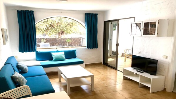 A living room with a sofa, a coffee table, a TV on a stand, and a sliding glass door leading to an outdoor area.