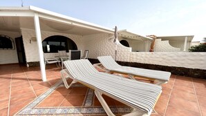 A covered outdoor seating area with two striped lounge chairs and a table, a tiled floor, and a white wall with a stone base. - Welooveyou Libra Starlight A42 (Costa Calma (incl. Urbanización Cañada del Río))