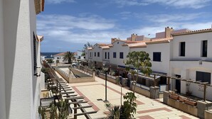 Eine Küstenstraße mit weißen Gebäuden, einem gefliesten Gehweg und Blick aufs Meer.