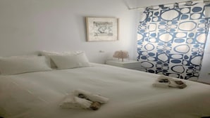 Ein ordentlich bezogenes Bett mit weißen Leinen und Handtüchern, ein Nachttisch mit Lampe und ein gemustertes Vorhang.