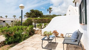 Une terrasse avec une table et une chaise, entourée de verdure et bordée d’un bâtiment blanc orné d’une plaque commémorative indiquant la date de construction.