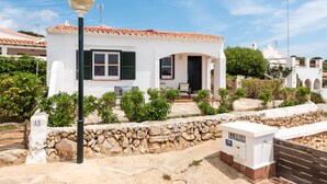 Une villa blanche avec un toit en tuiles, un mur en pierre et un petit jardin.