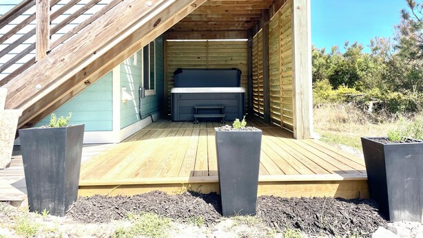 A wooden deck with a bench, a hot tub, and a staircase leading to a covered area. - Romantic Little Getaway in 4X4 beach (Corolla)